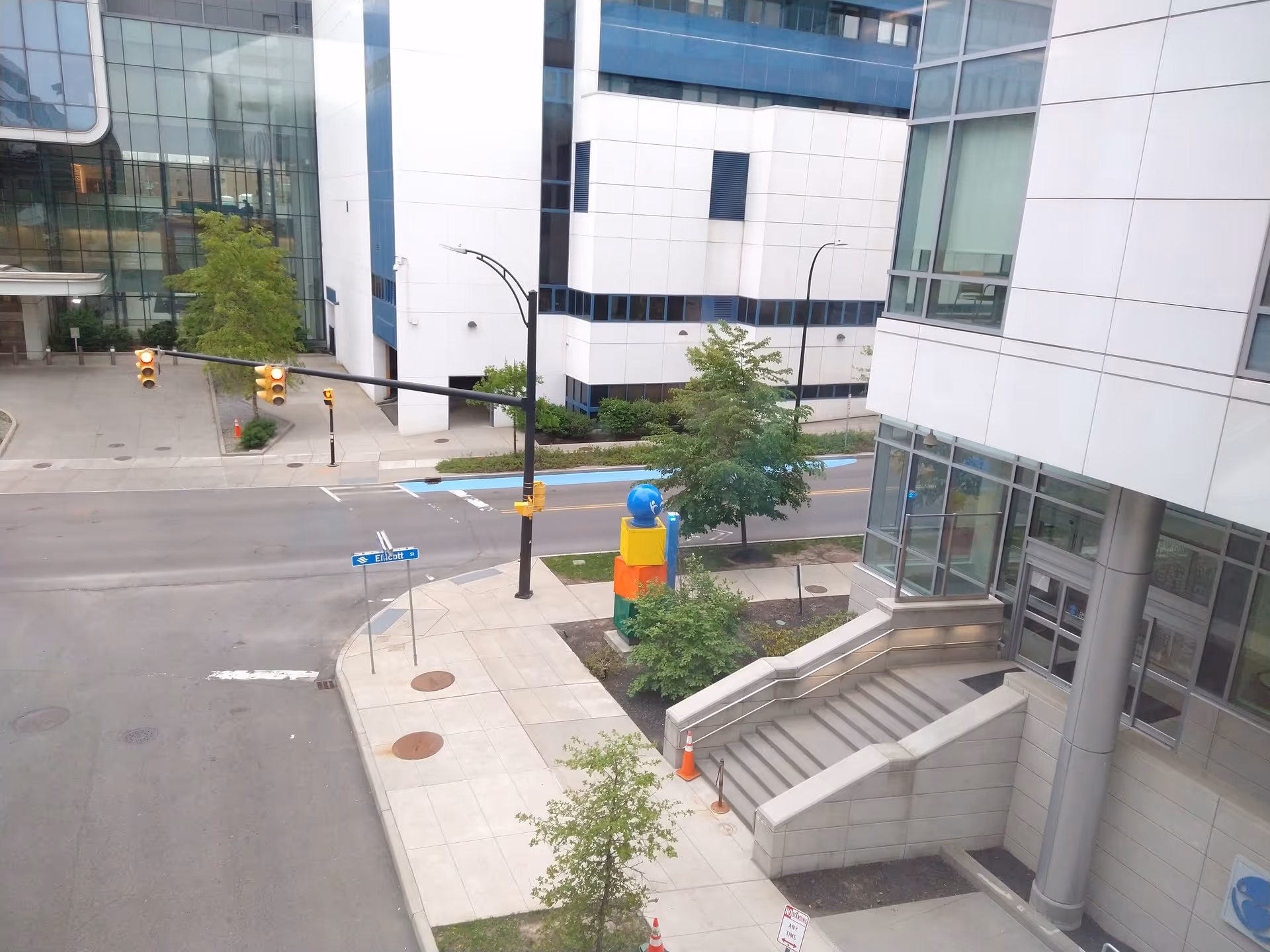 A modern city street scene with a glass building and colorful stacked sculpture.