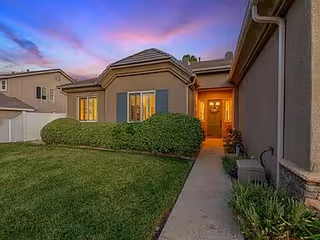 A single-story senior living building with a lit entry door and manicured lawn.