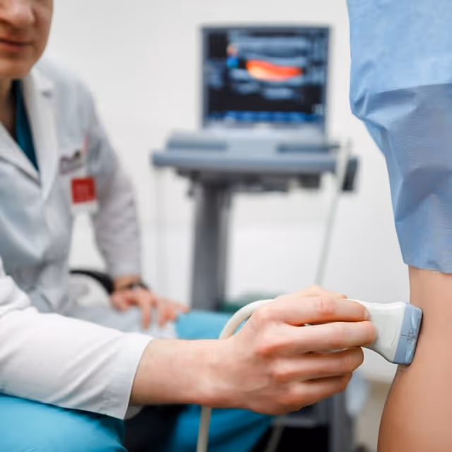 Medical professional uses ultrasound probe on a patient's arm in a clinical setting.