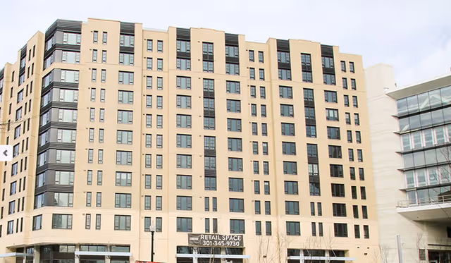 Front of a tall beige multi-story building with numerous windows and a ground-floor retail space.