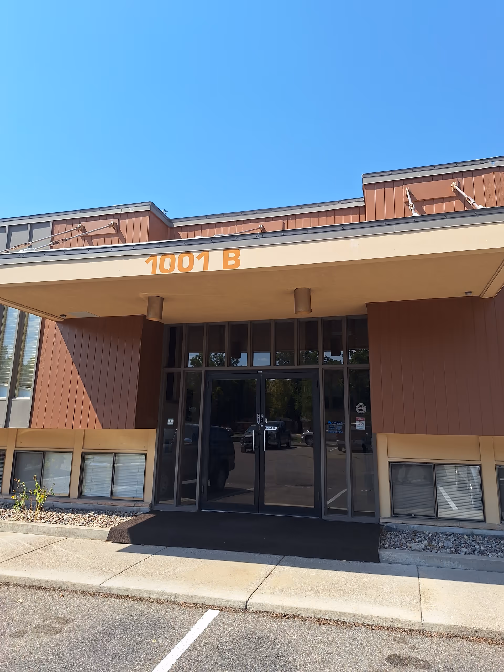 Front entrance of a building with glass doors, brown facade, and 1001 B above.