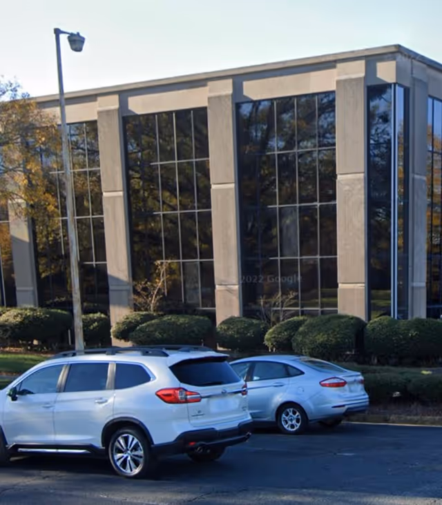 Exterior view of a modern glass-front building with a parking lot and cars