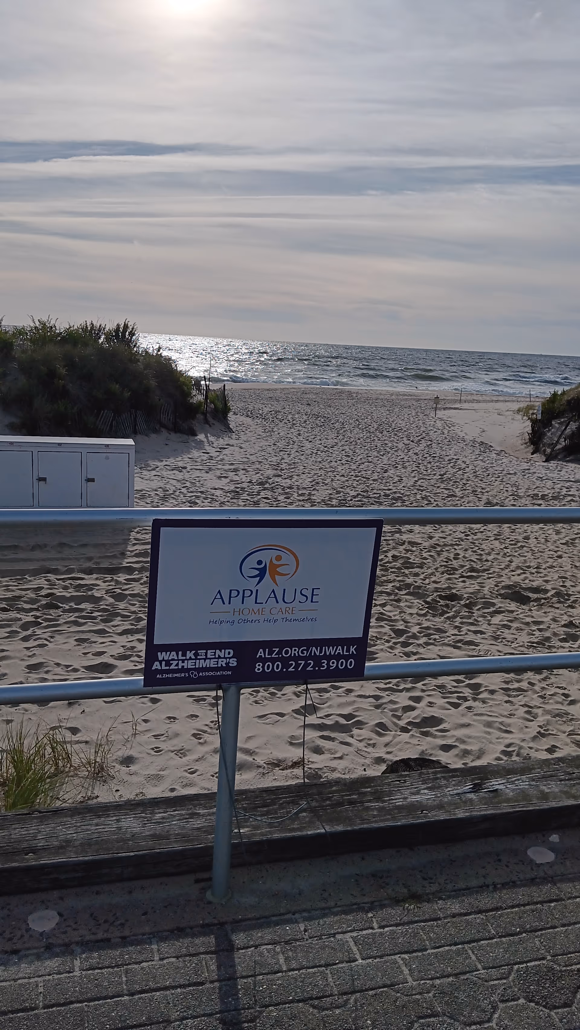 Sign for Applause Home Care beside a sandy beach boardwalk.