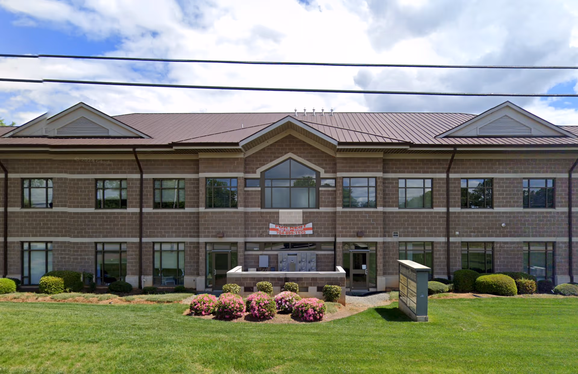 Two-story brick building with manicured lawn and flowering shrubs in front.
