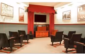 A small communal lounge with rows of chairs, red curtains, stage, and television.