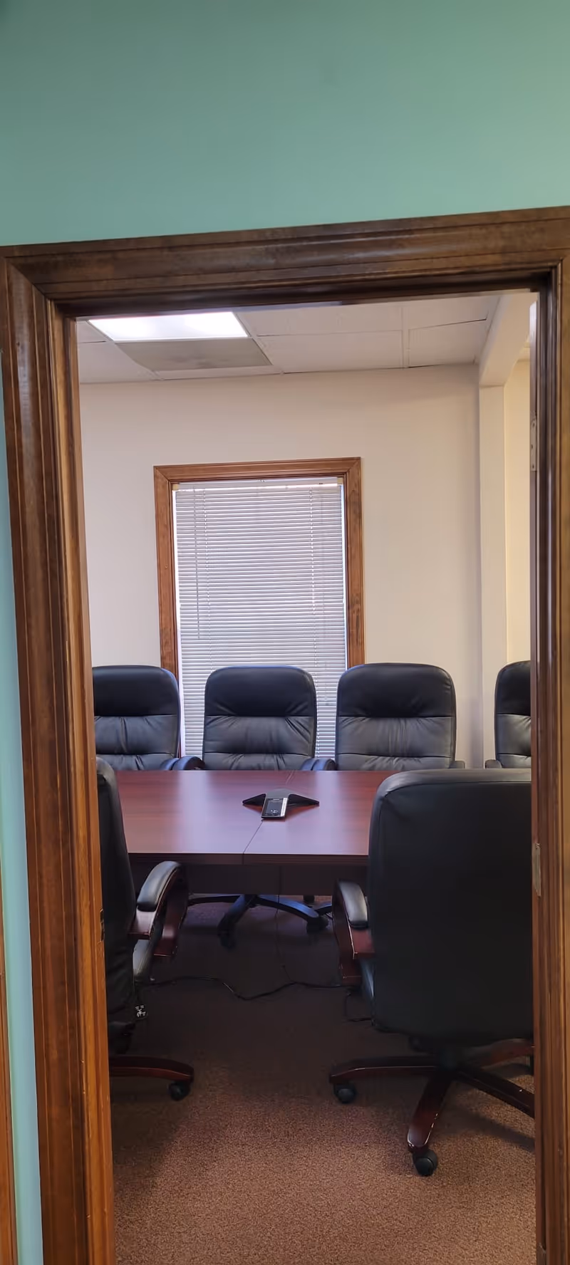 Indoor conference room with a long table, black chairs, and window blinds.