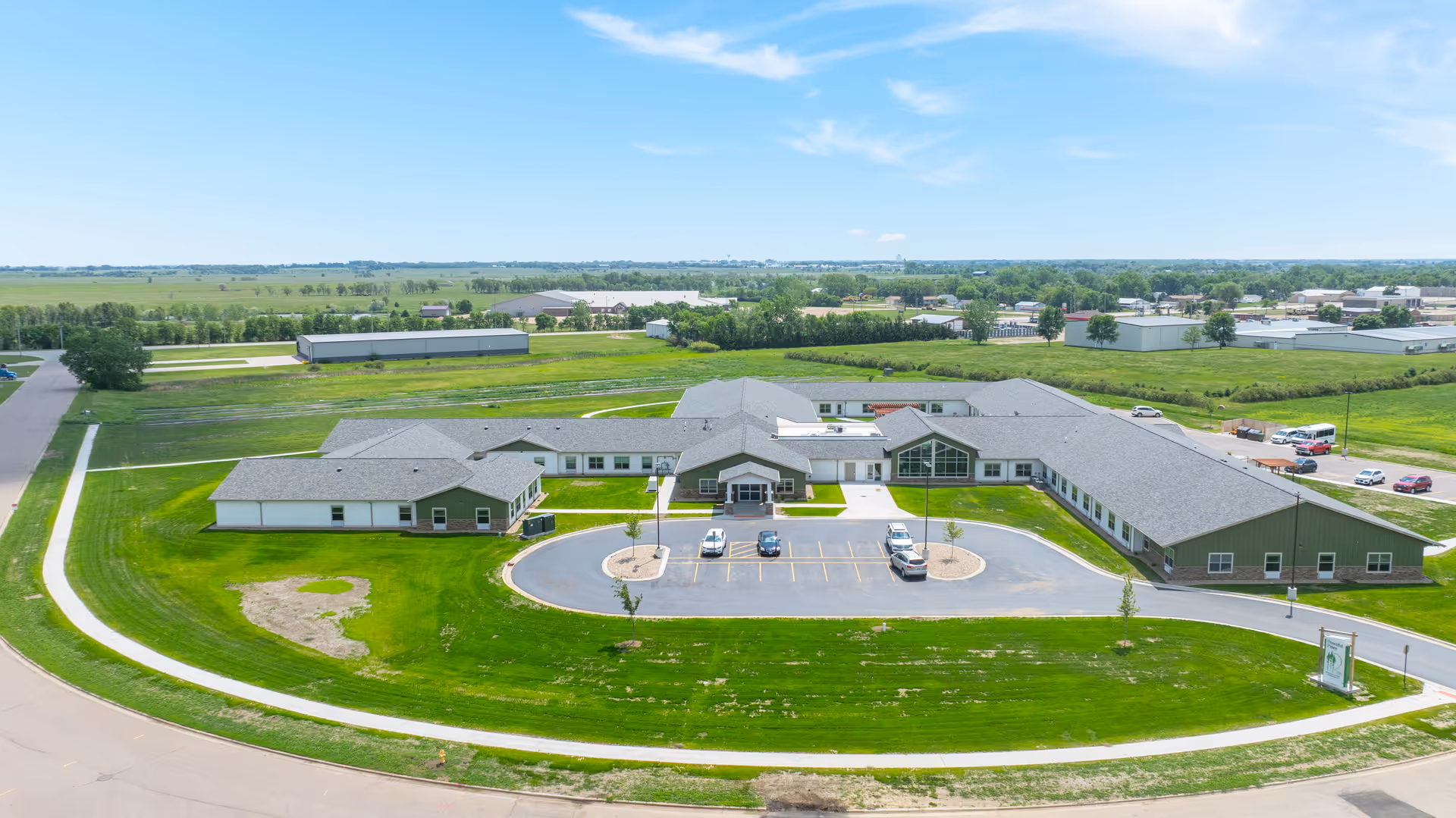 Aerial view of a large senior living campus with green lawns, ample parking, and low-rise buildings.