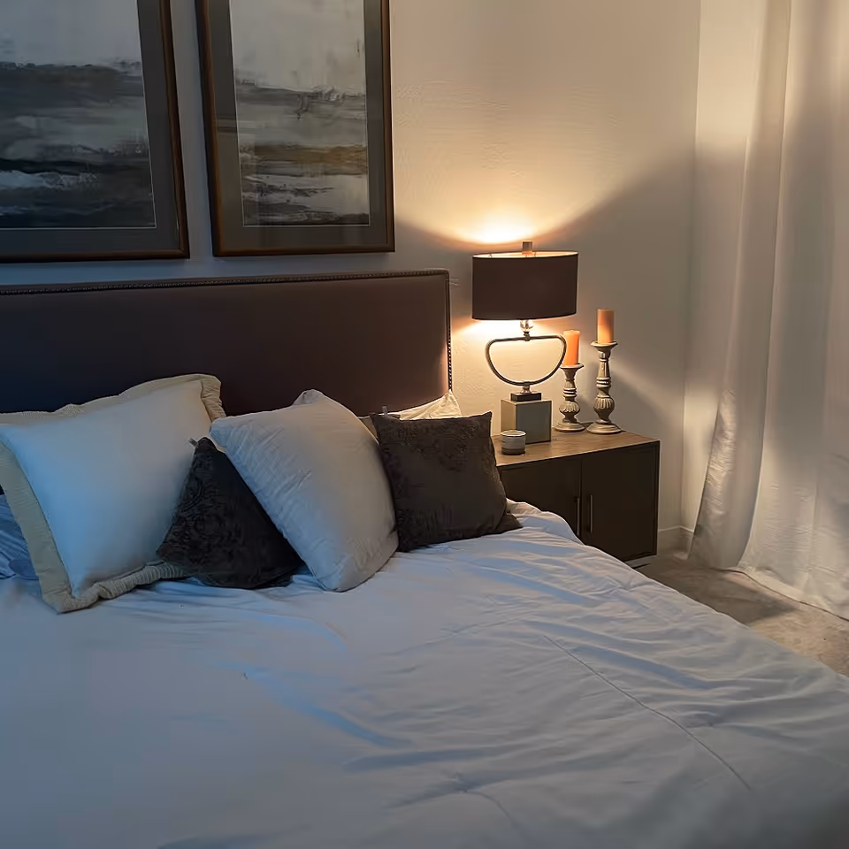 A neatly made bed with white sheets and multiple pillows in a softly lit bedroom.