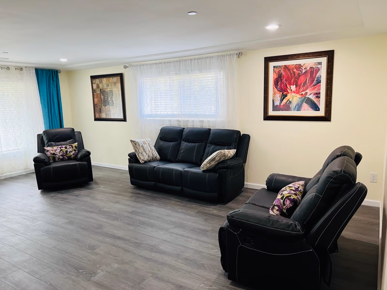 Spacious living room with black leather recliners, a sofa, cushions, and framed art.