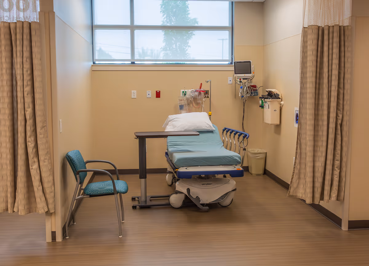 Hospital-style patient bed with curtains and medical equipment in an examination room.