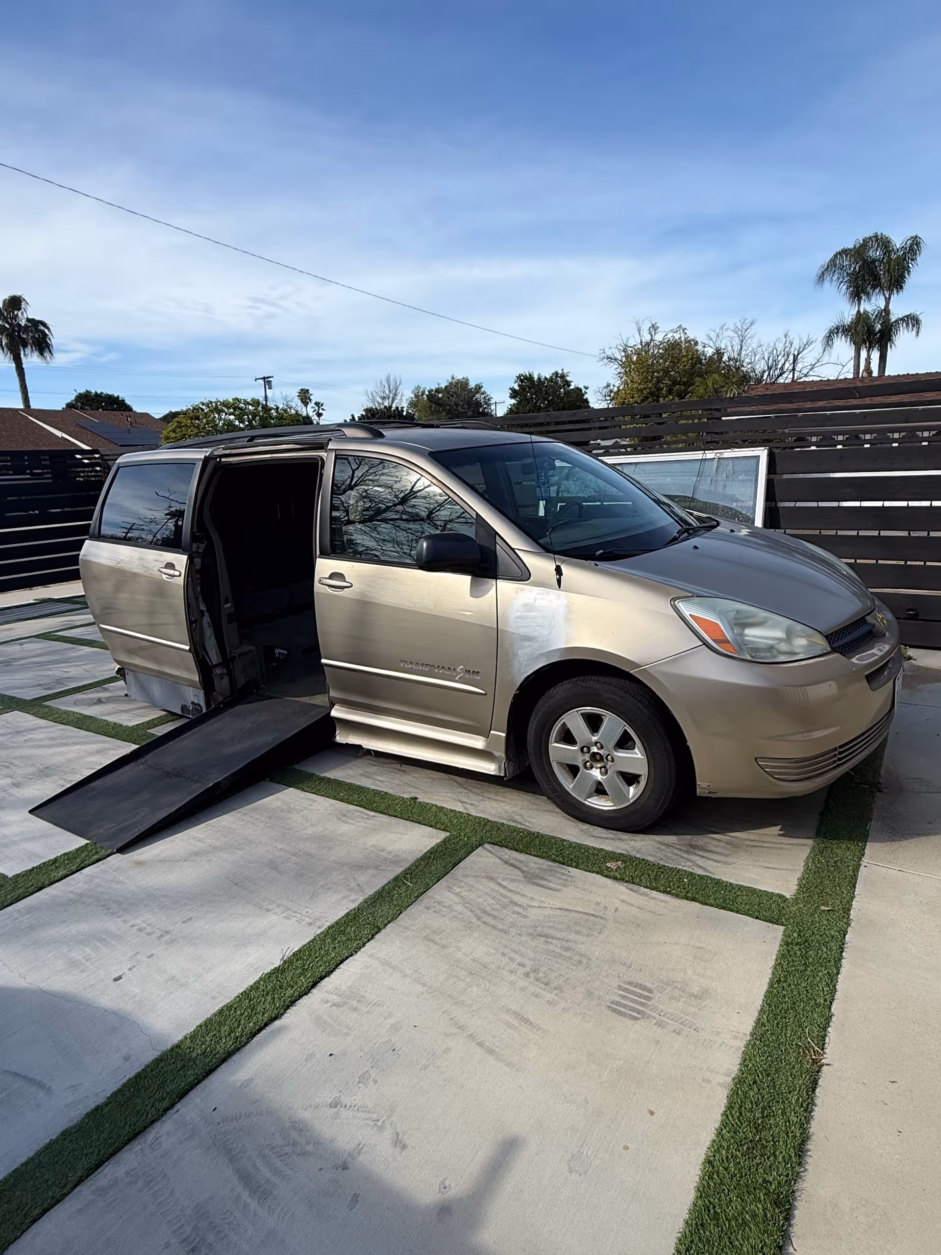Minivan with a lowered ramp sits on a paved driveway.