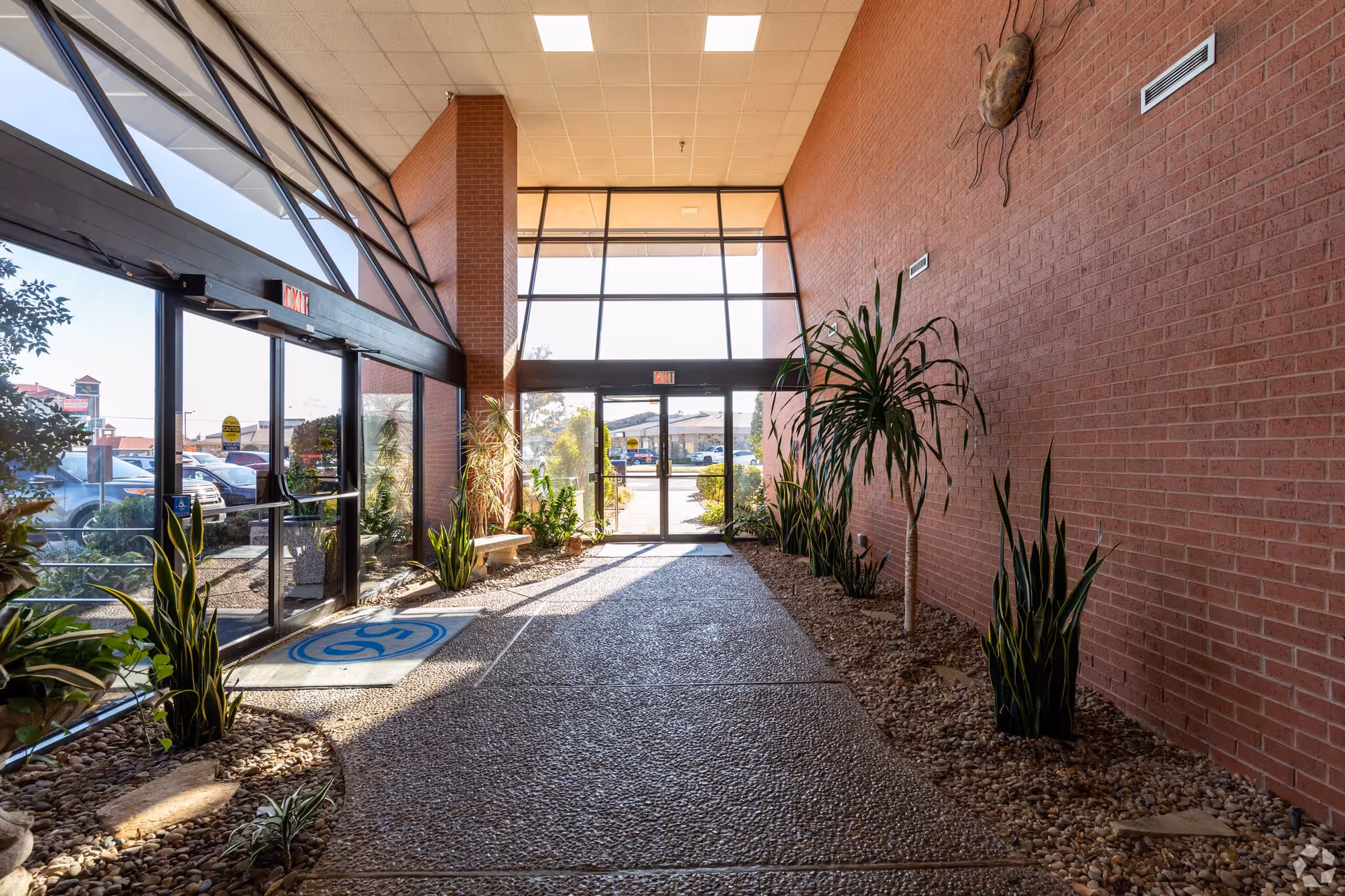 Bright indoor atrium-style entrance with glass doors, brick walls, and potted plants.
