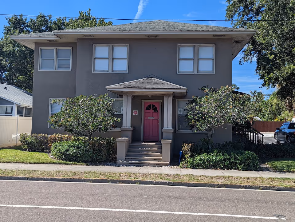 Two-story gray building with a pink front door and steps to entry.