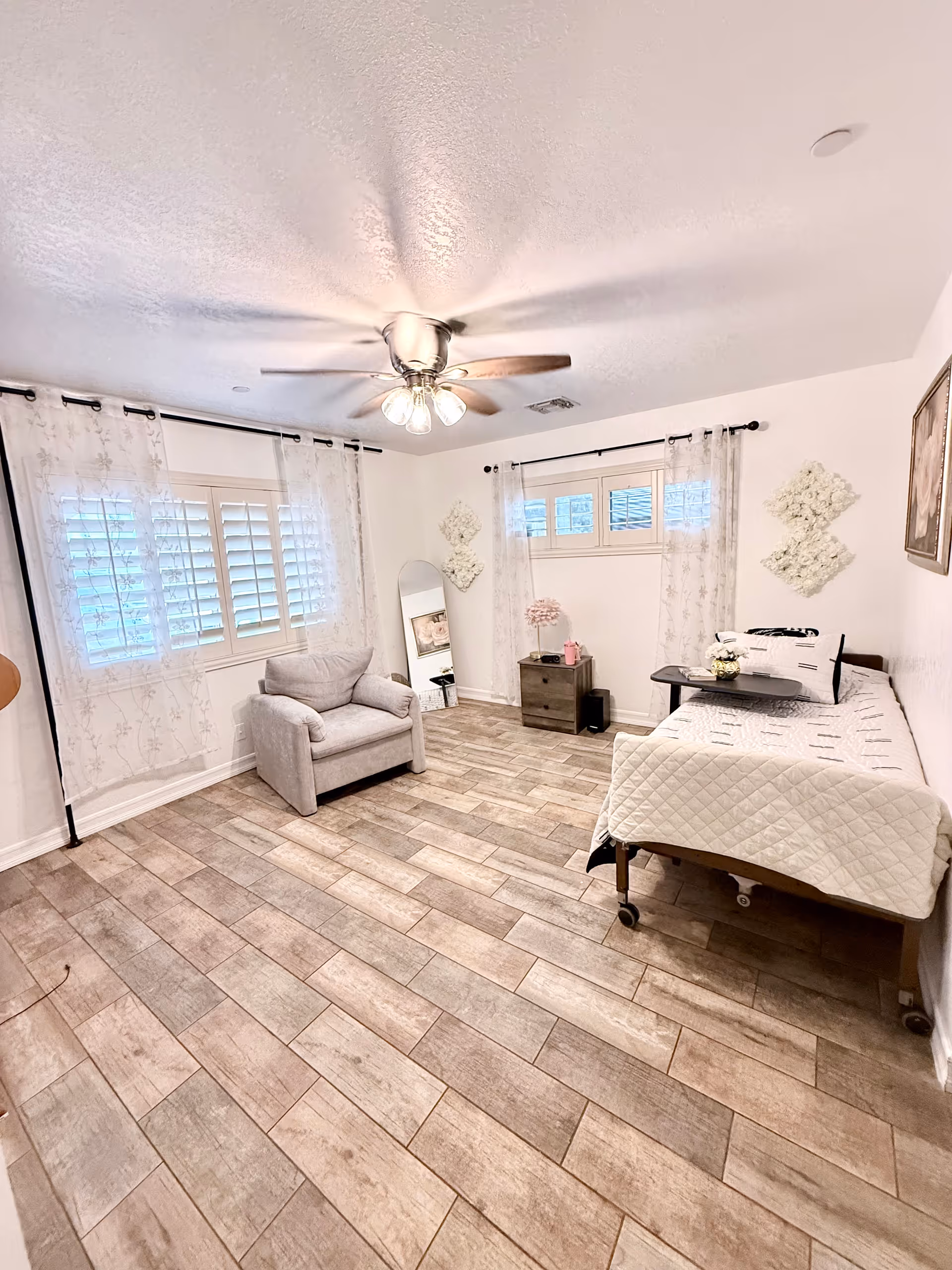A tidy senior living bedroom with a hospital-style bed, chair, and windows.