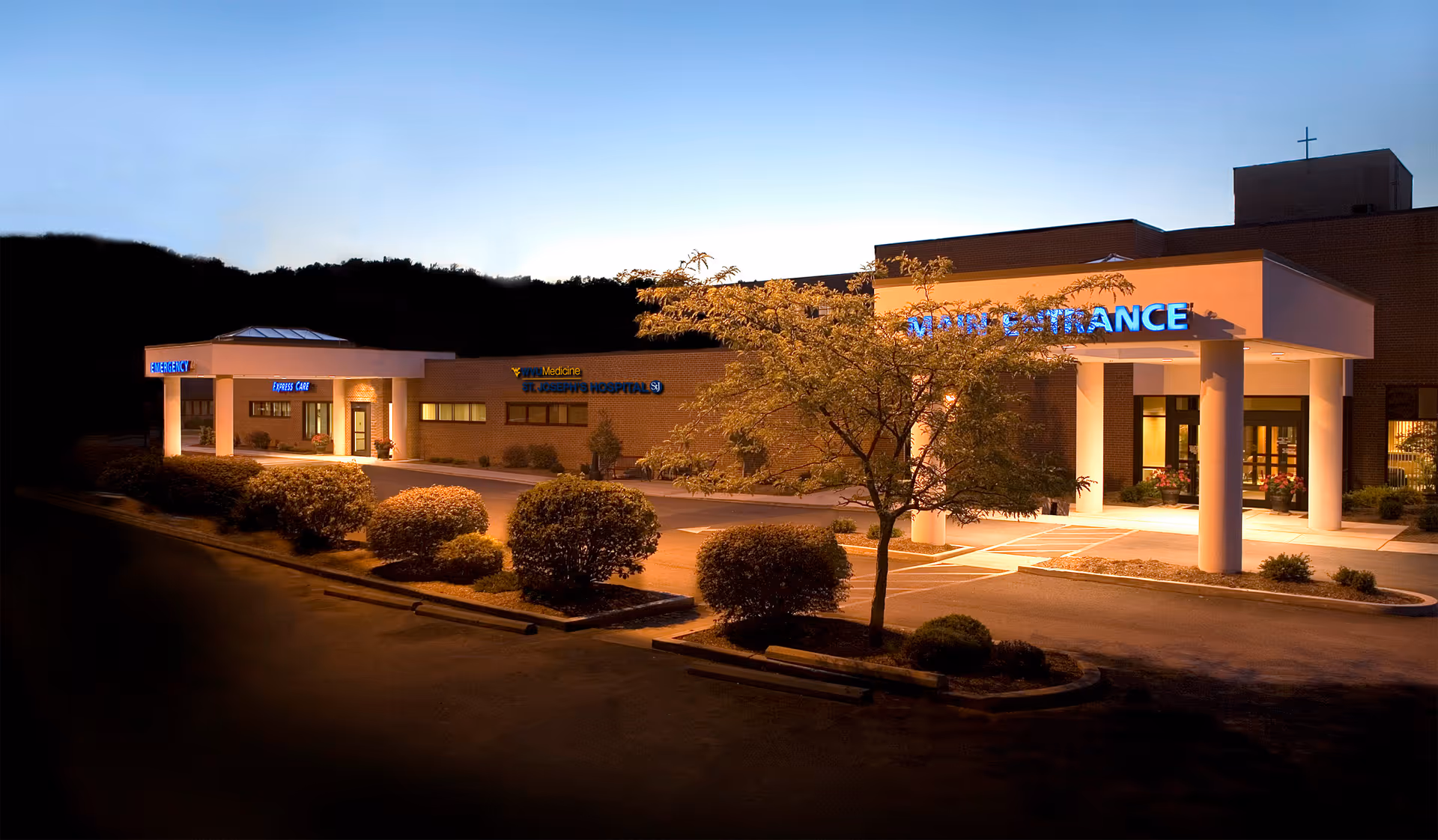 Exterior view of a hospital building at dusk with a bright main entrance and landscaping.