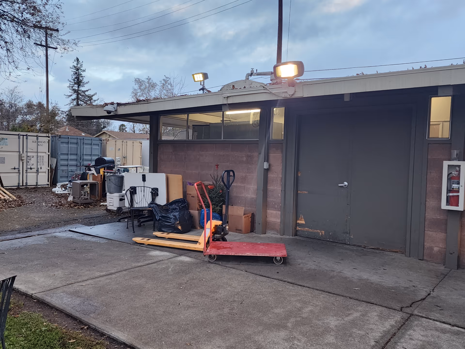 Outdoor loading area next to a brick building with pallets, equipment, and a door.
