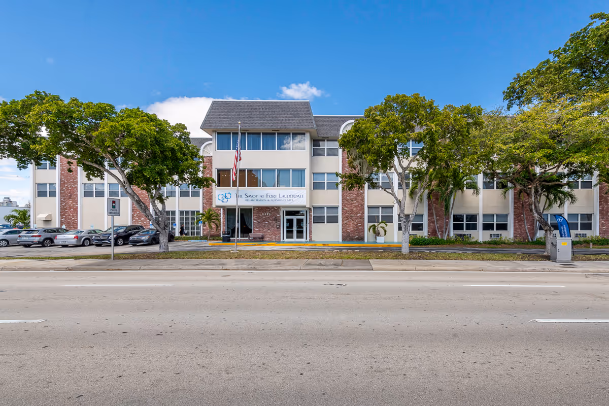 Exterior view of The Savoy at Fort Lauderdale building with trees, cars, and entrance.