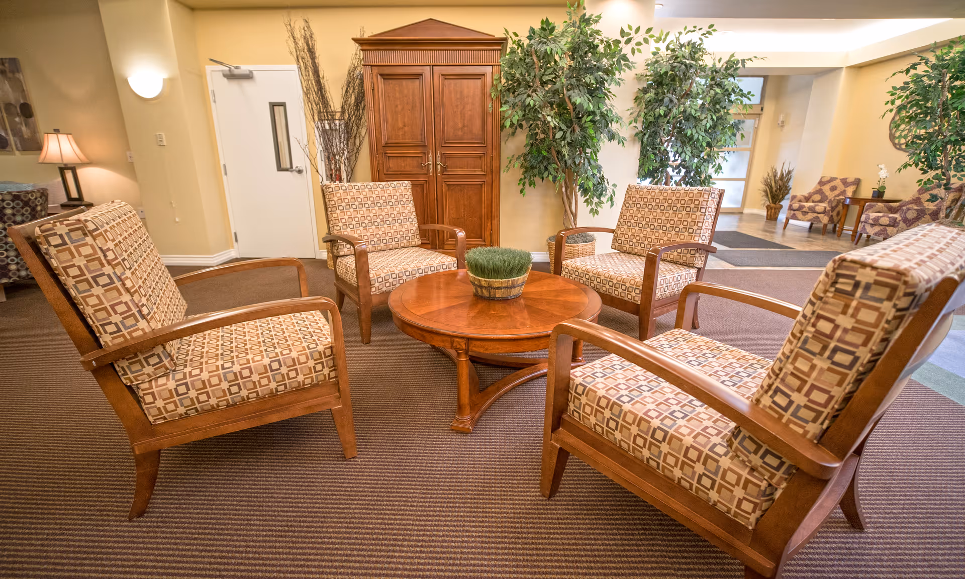 A lounge area with four patterned cushioned armchairs around a round wooden table.