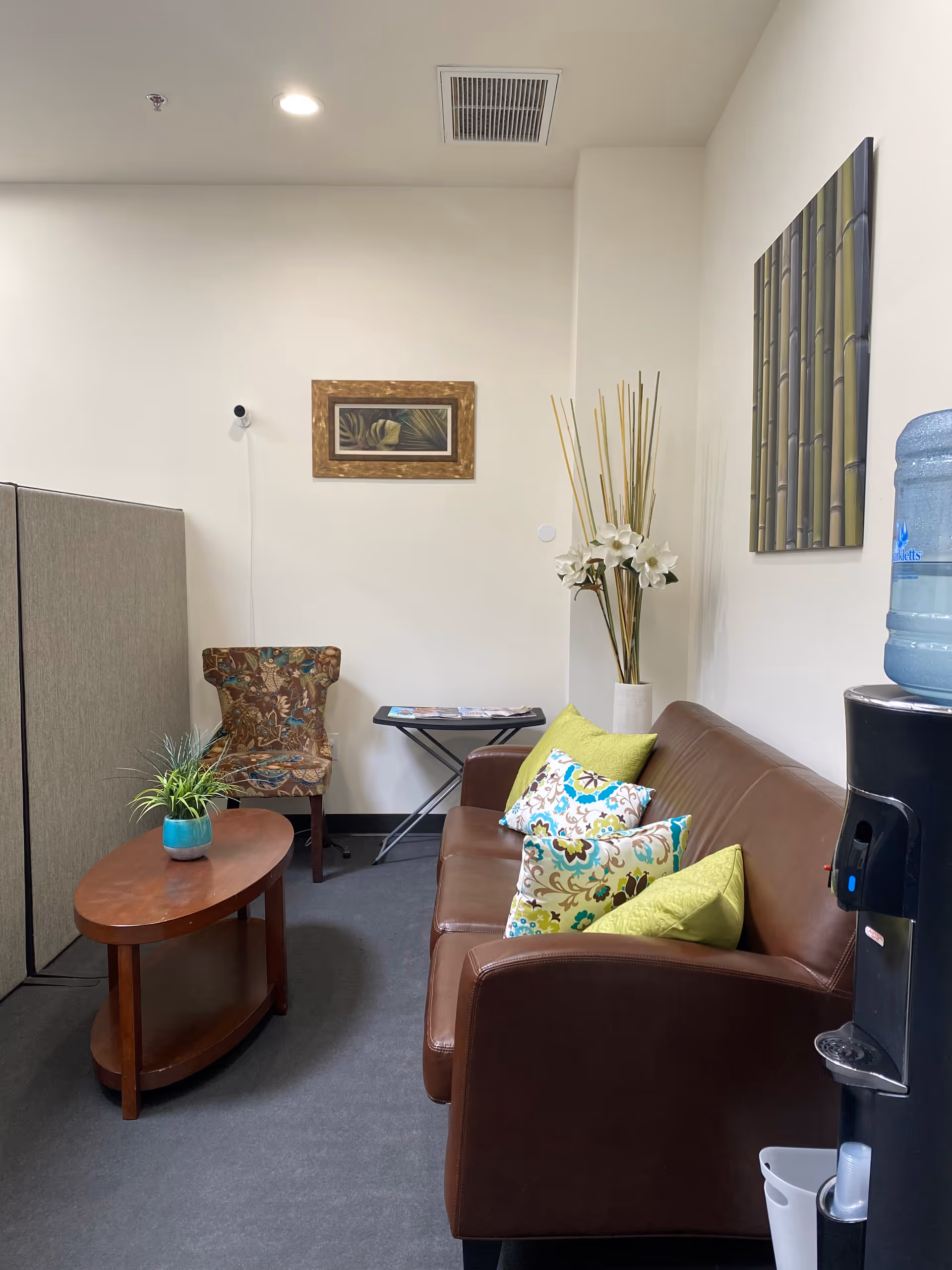 Cozy senior living lounge with brown leather sofa, colorful cushions, coffee table, and water cooler.