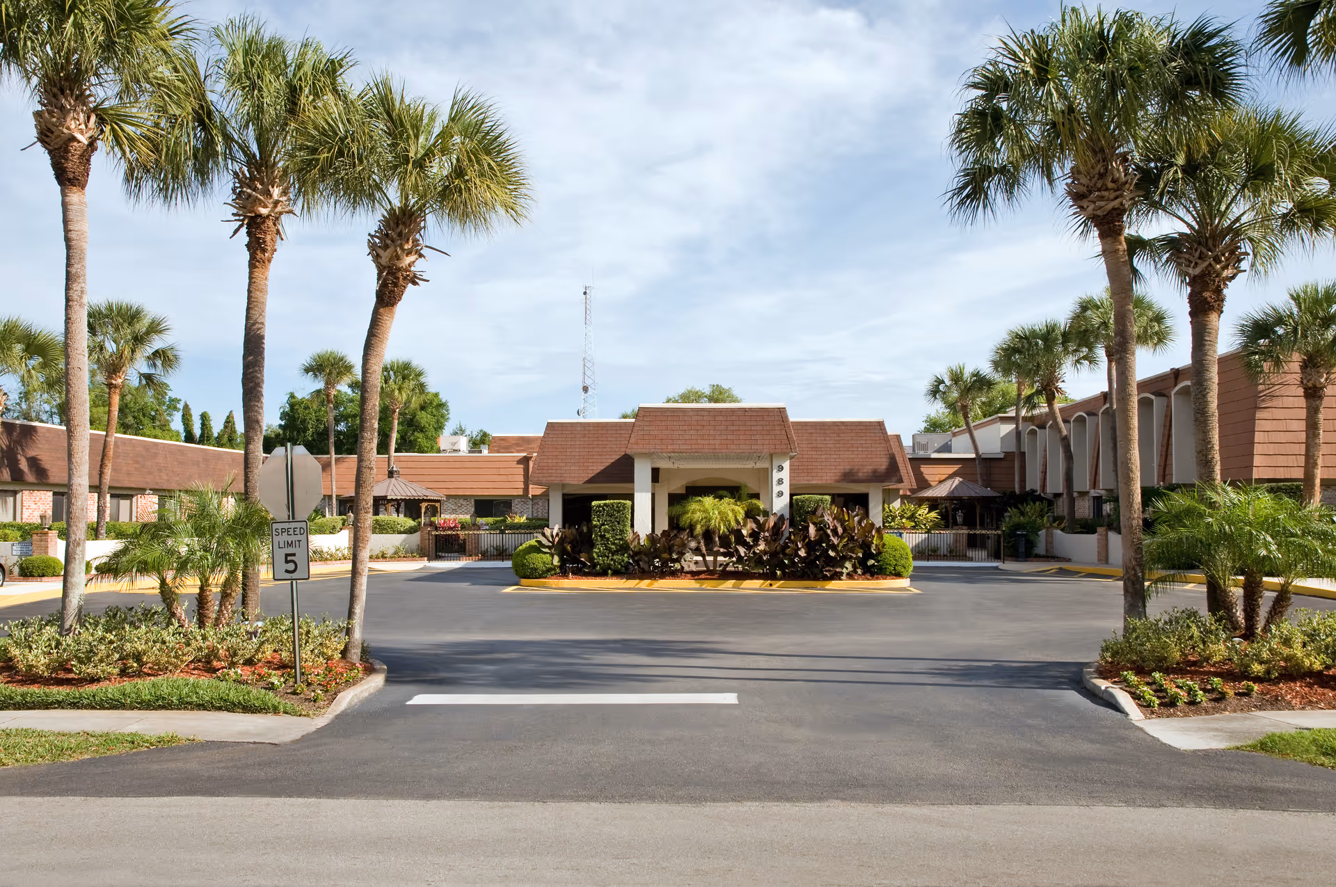 Exterior view of a senior living center entrance with a driveway and palm trees.