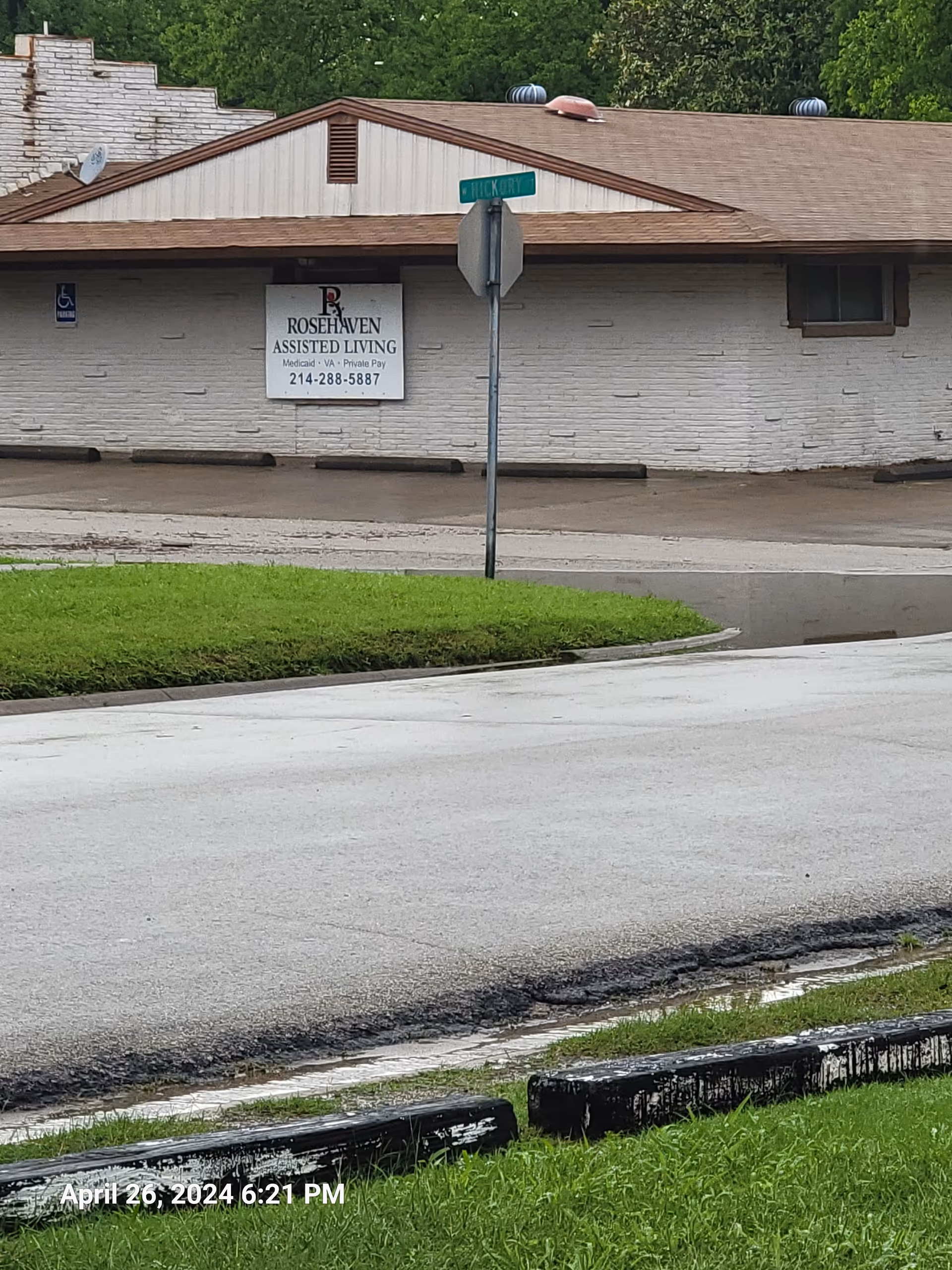 Front exterior of a single-story assisted living building with a street sign and curb.