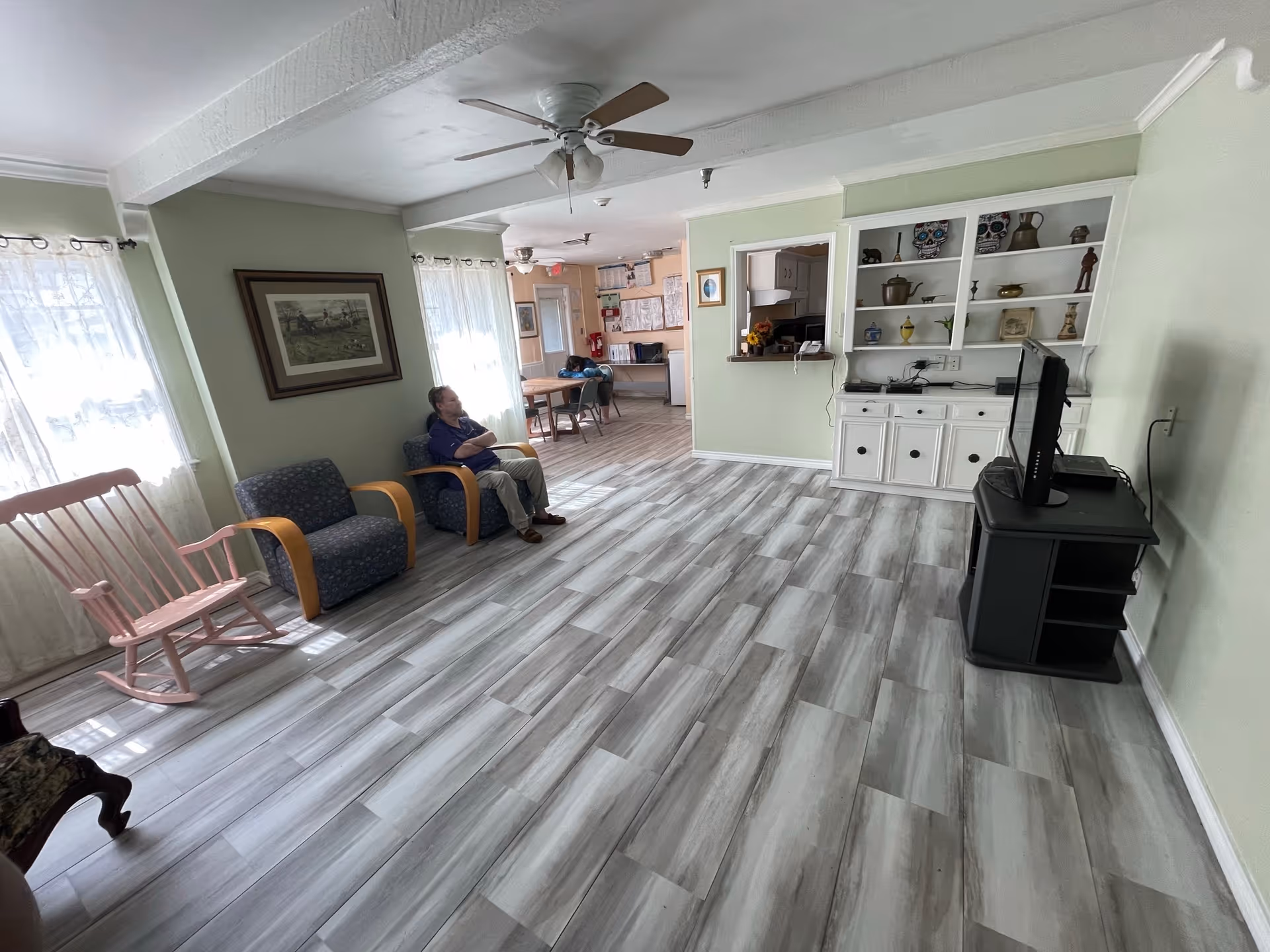 Spacious lounge in a senior facility with seating, a TV stand, and decorative shelves.