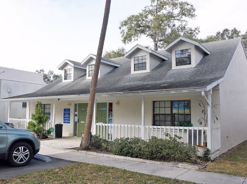 Exterior view of Oasis Temps Healthcare facility with white building, porch railing, and a palm tree.