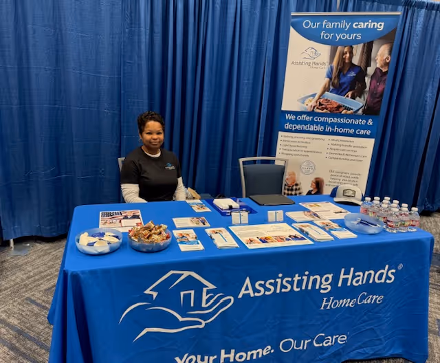 Staff member sits at a blue promotional table for Assisting Hands Home Care Cypress.
