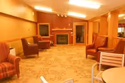 Cozy senior living lounge with armchairs, tables, and a fireplace.