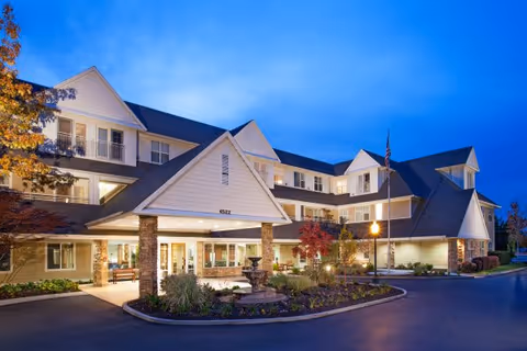 Exterior view of The Wellington senior living facility with entrance, landscaping, and fountain.
