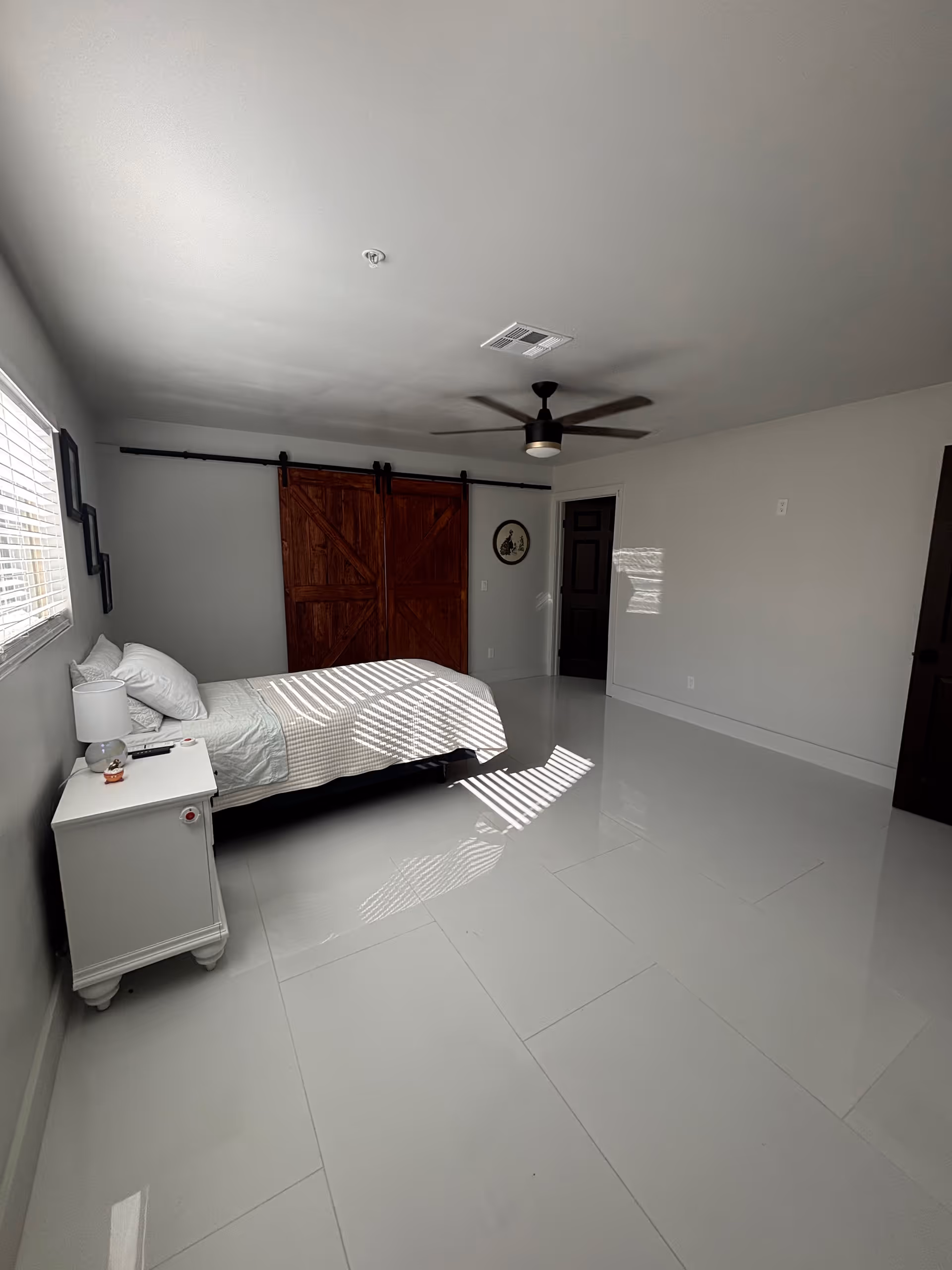 A bright bedroom with a bed, nightstand, ceiling fan, and sliding barn door.