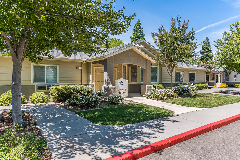 Front exterior of a single-story senior living facility with manicured landscaping and a walkway.