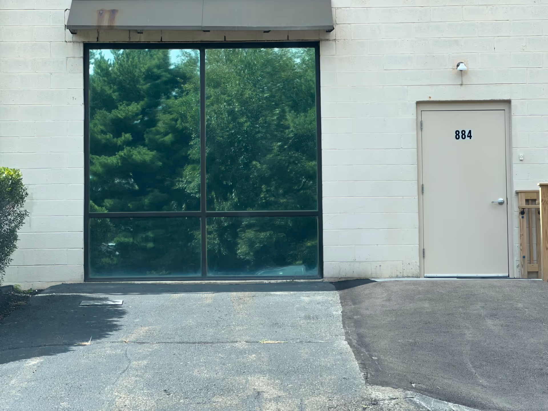 Exterior of a light brick building with a large glass window and a numbered entry door.