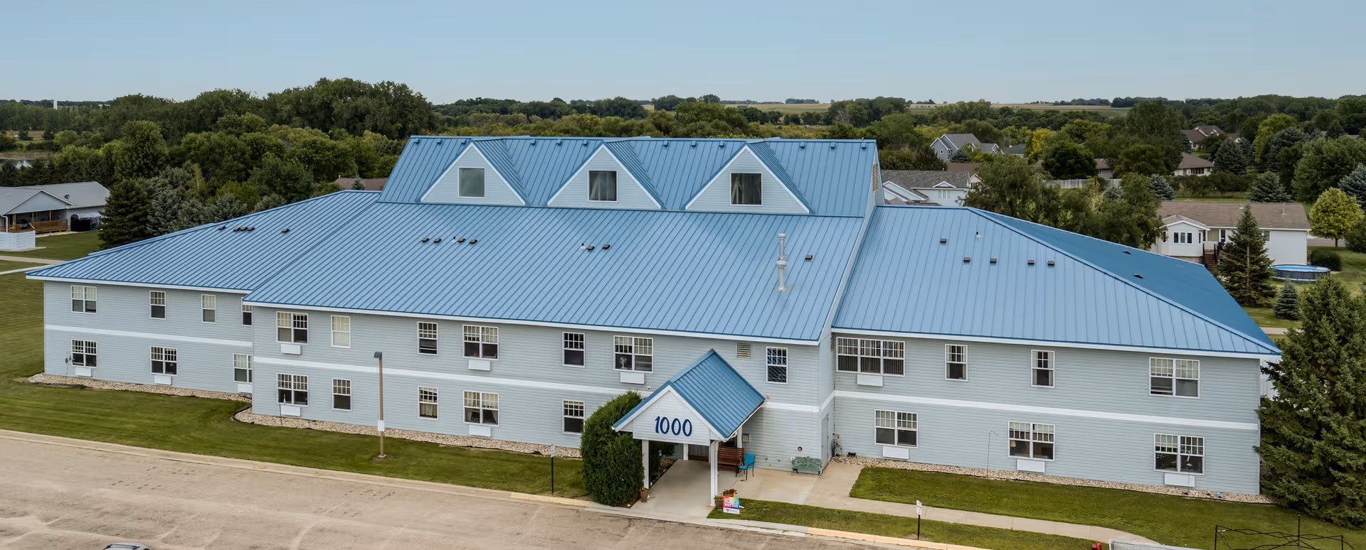 Blue-roofed, two-story senior living building with numerous windows and green lawn.