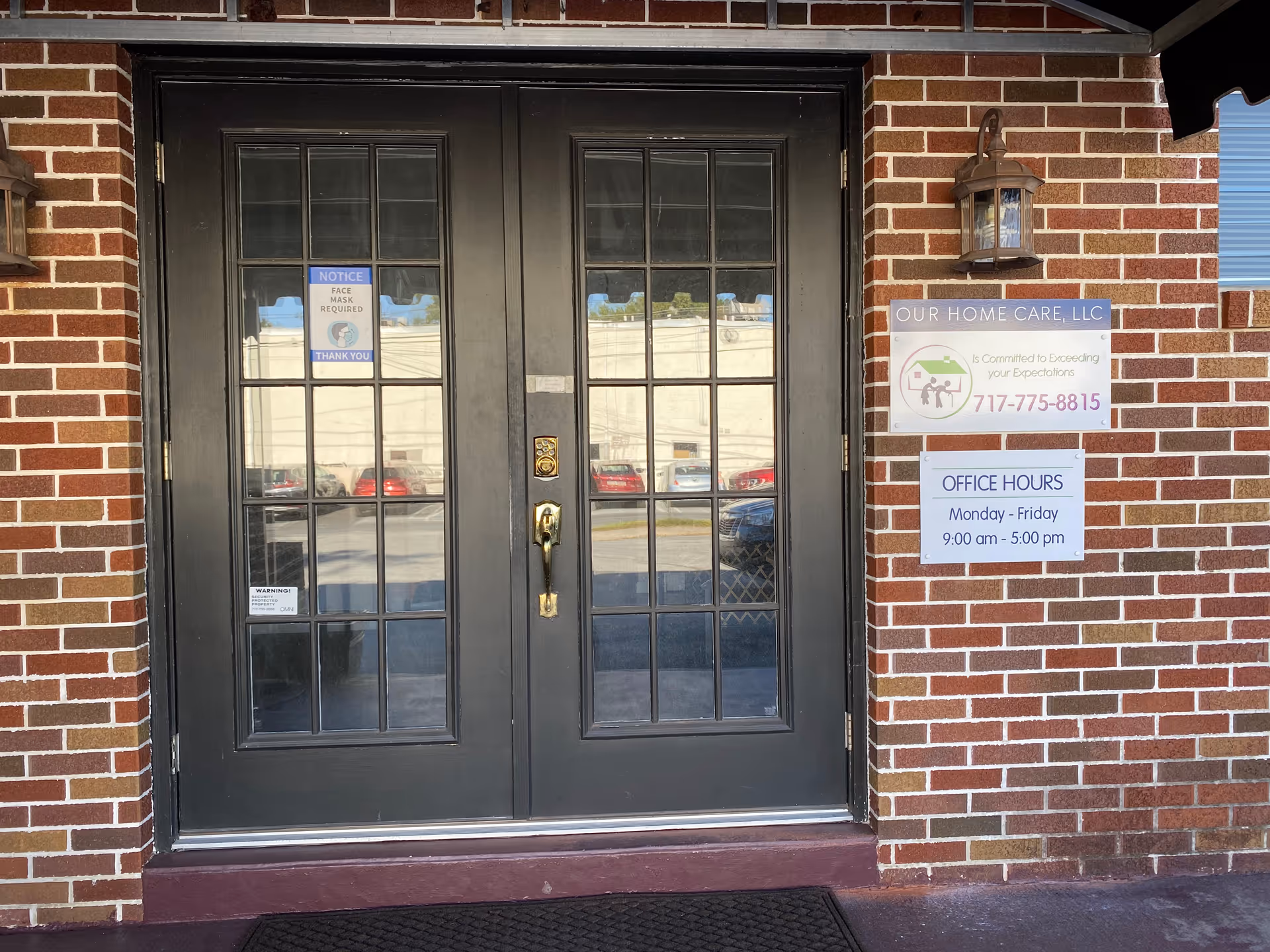 Brick building entrance with black double doors and posted signs.