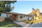 Single-story building with entrance, American flag, manicured lawn, and palm trees in daylight.