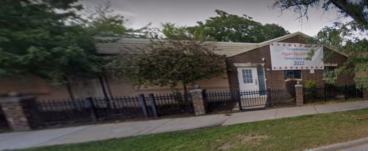 Exterior view of Algart Health Care Inc. building with a banner, fence, and trees.