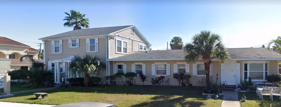 Front exterior of a beige two-story and adjoining single-story residential building with palm trees, a lawn, and a concrete walkway.
