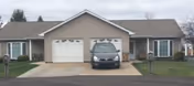 Front view of a one-story duplex-style building with two attached garages, a car parked in the center driveway, and small lawns and mailboxes.