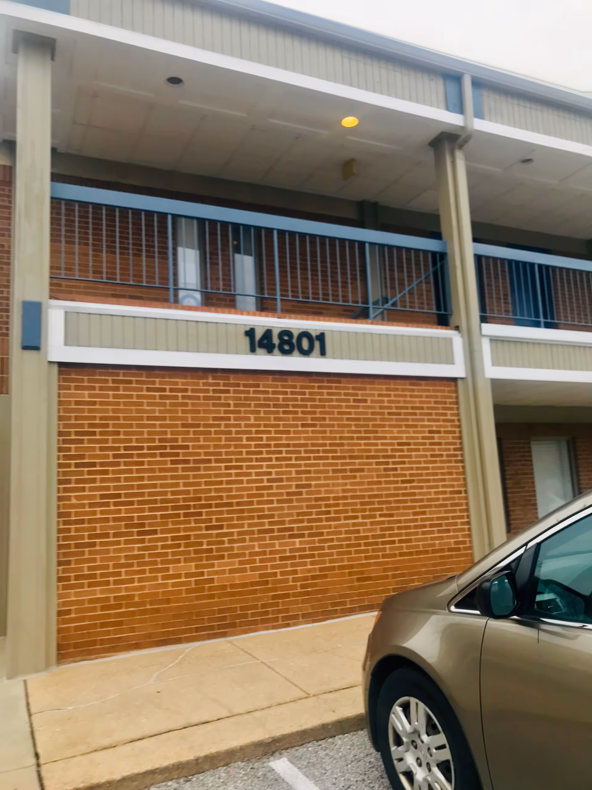 Exterior view of a brick senior living facility with balcony and a parked car.
