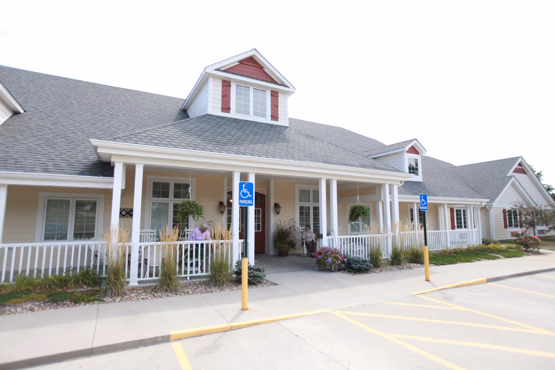 Front entrance of a single-story assisted living building with a covered porch, wheelchair parking signs, and landscaping.