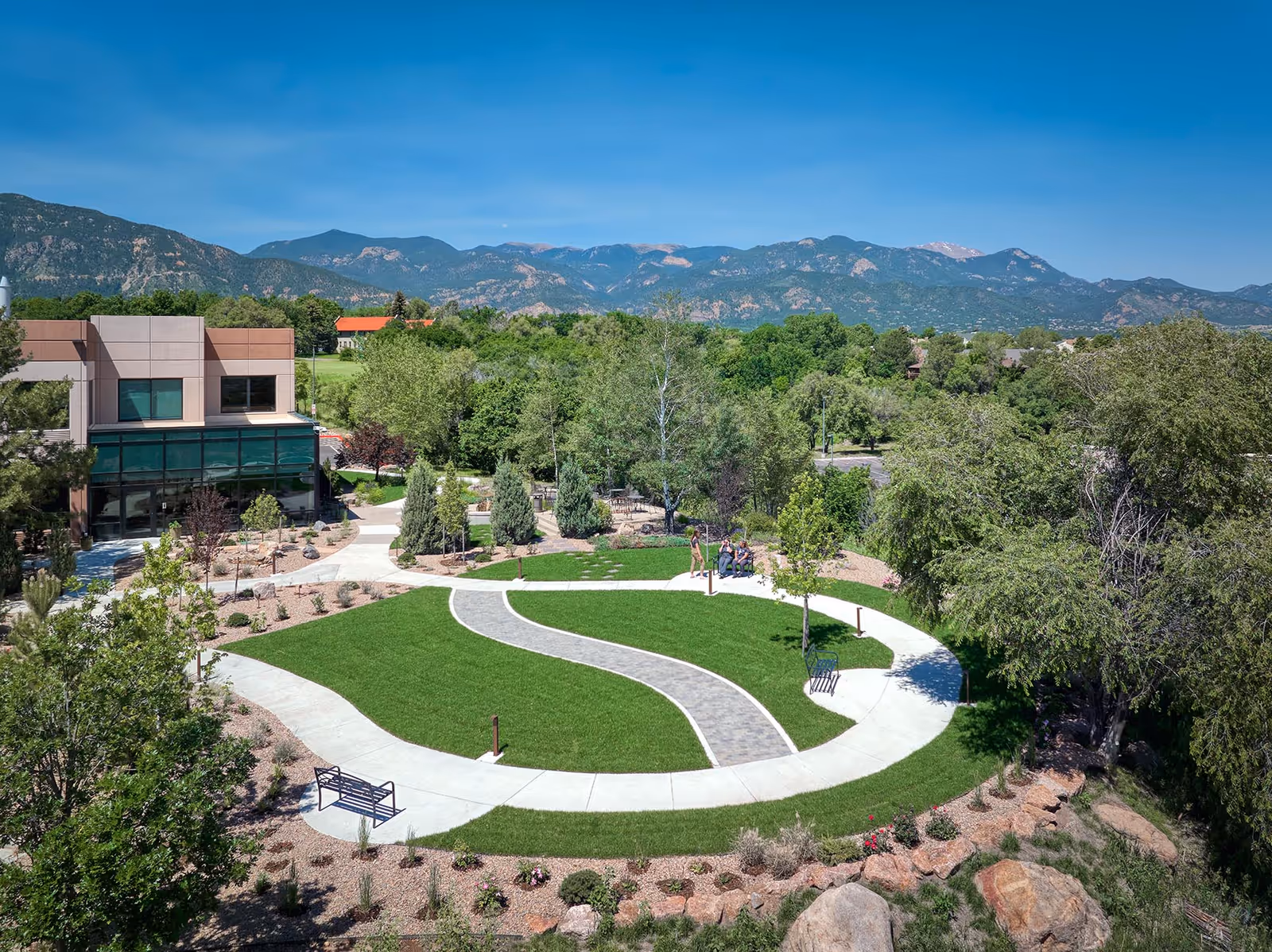 Aerial view of a landscaped outdoor courtyard with winding paths, benches, trees, and a building.