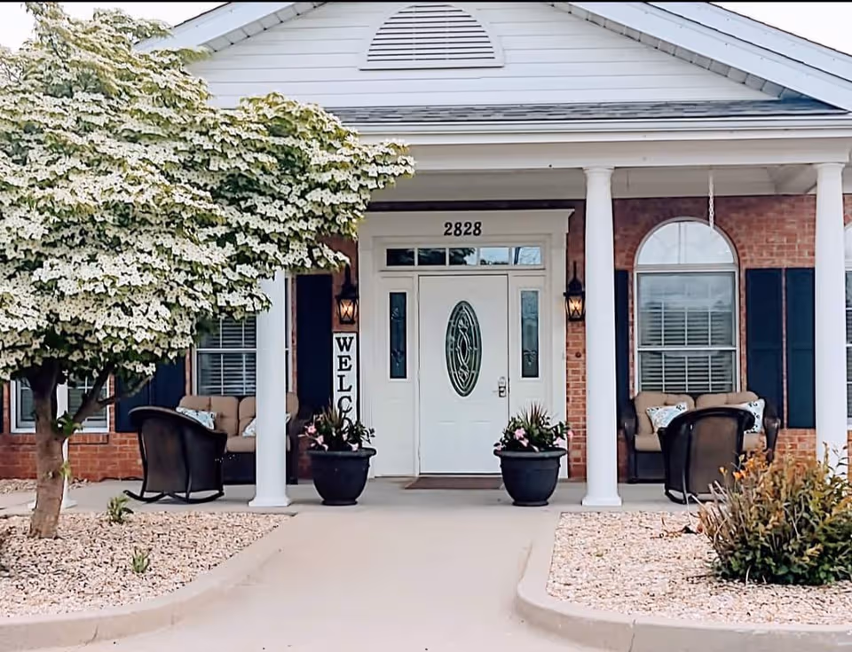 Front entrance of Spring Ridge Assisted Living with porch seating and potted plants.