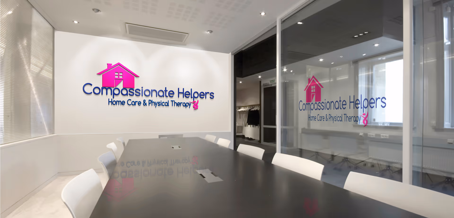 Interior conference room with a long dark table, white chairs, and Compassionate Helpers logo on wall.