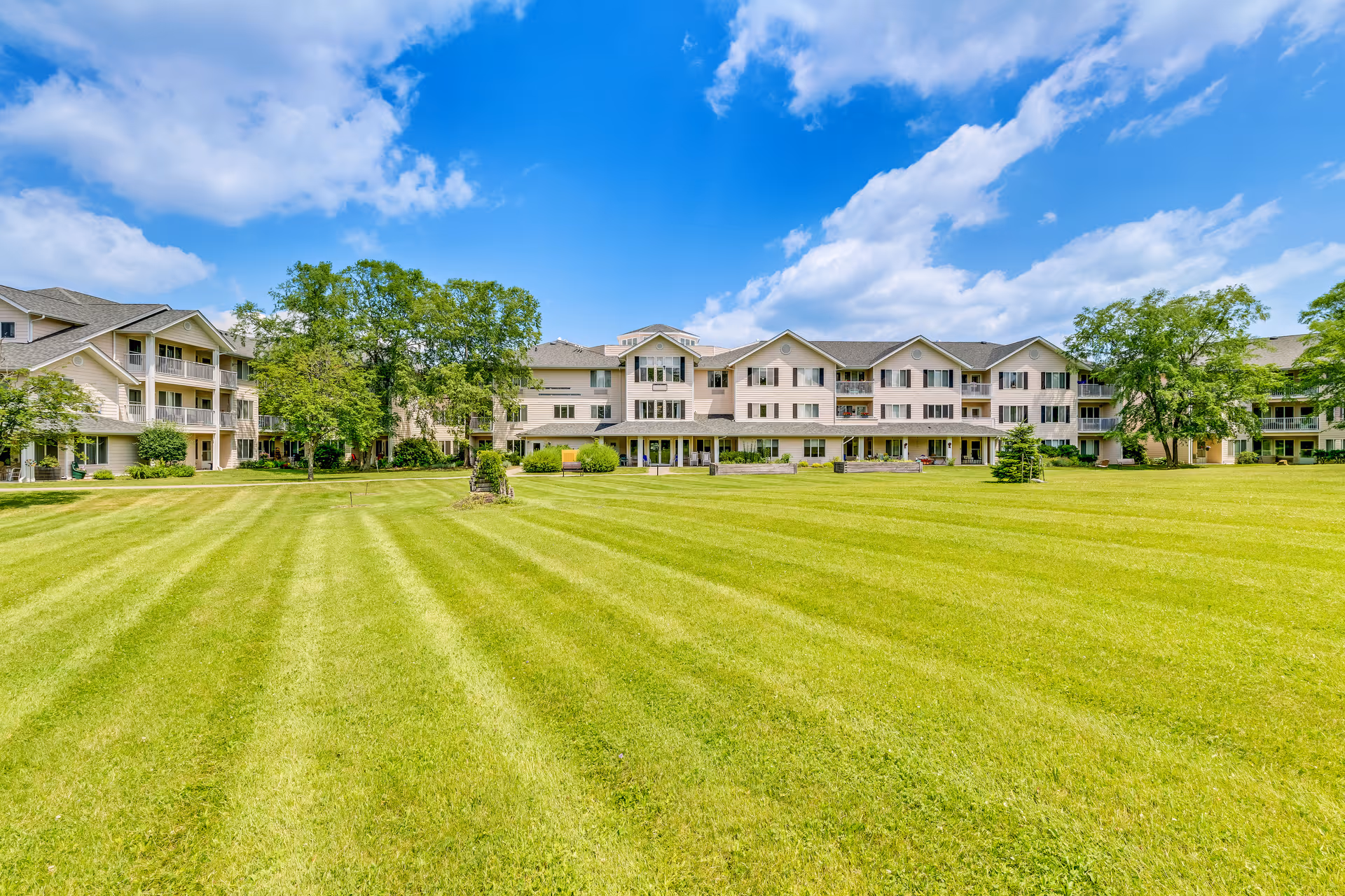 Wide view of a multi-wing senior living building with a manicured lawn and blue sky.