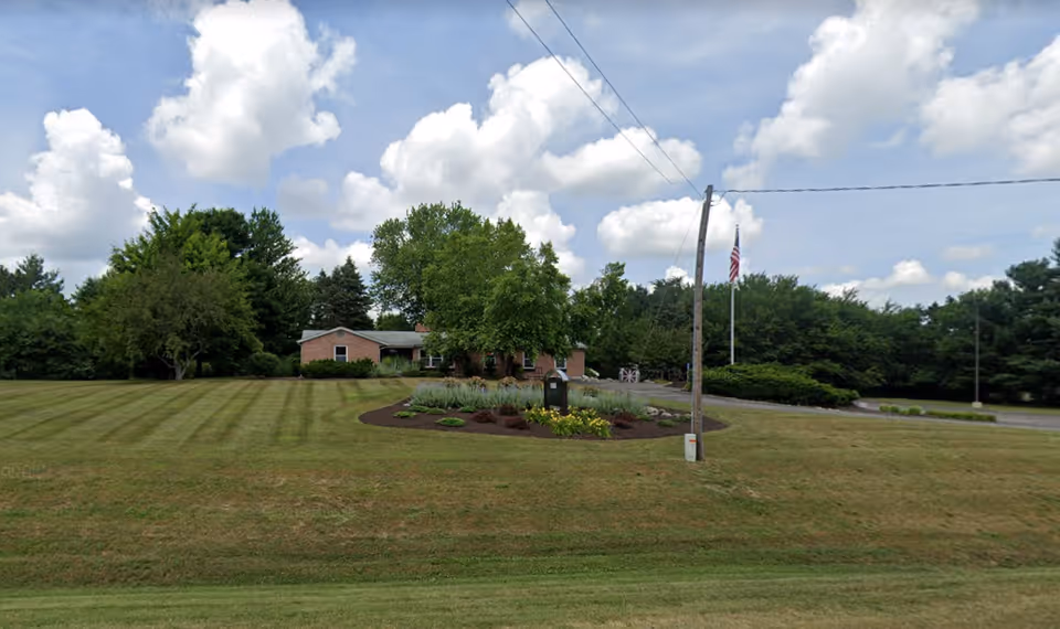 Brick senior living facility with circular driveway, flagpole, and manicured lawn.