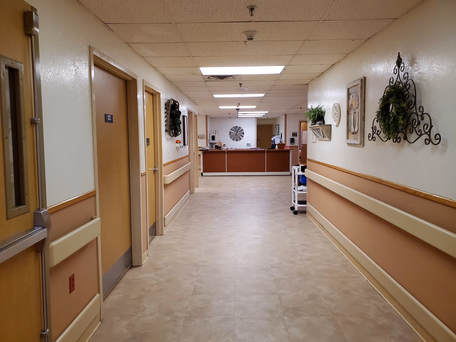 Long hallway inside a senior living facility with doors on both sides and a front desk.