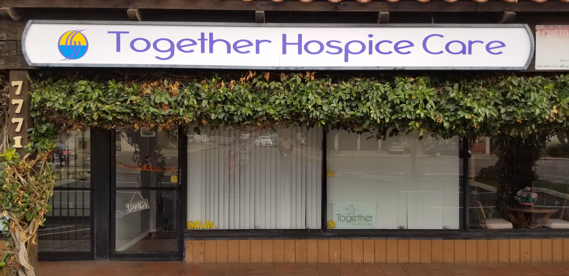 Exterior storefront with a sign reading Together Hospice Care and greenery.
