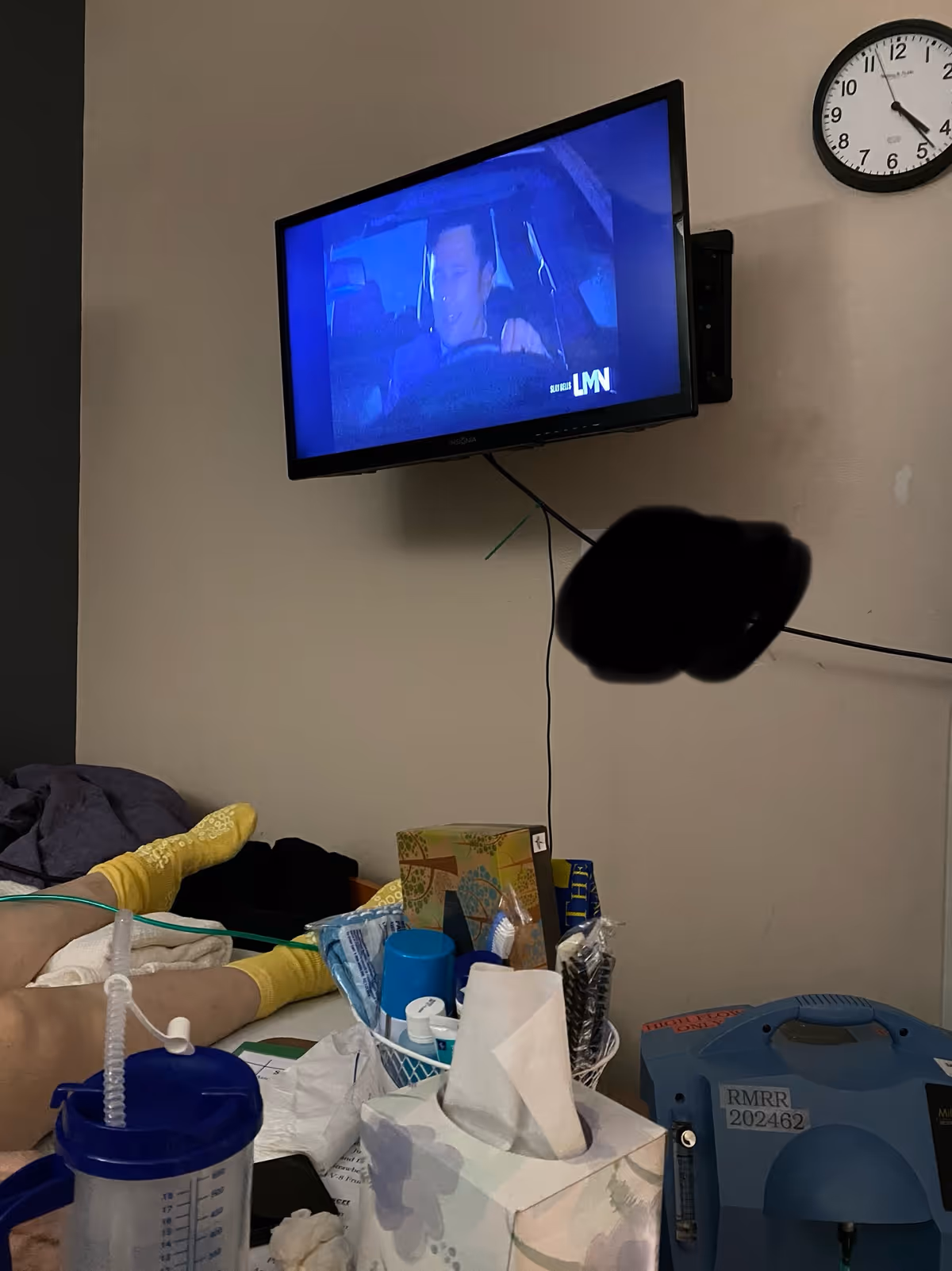 Patient resting in a post-acute room with mounted TV and bedside supplies.