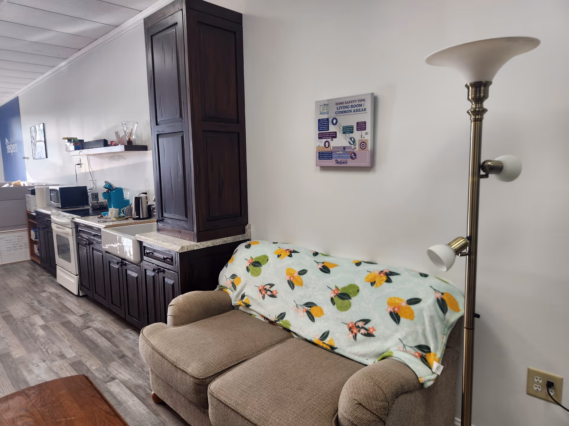 Cozy kitchenette and seating area with dark cabinets, lamp, and lemon-patterned blanket.